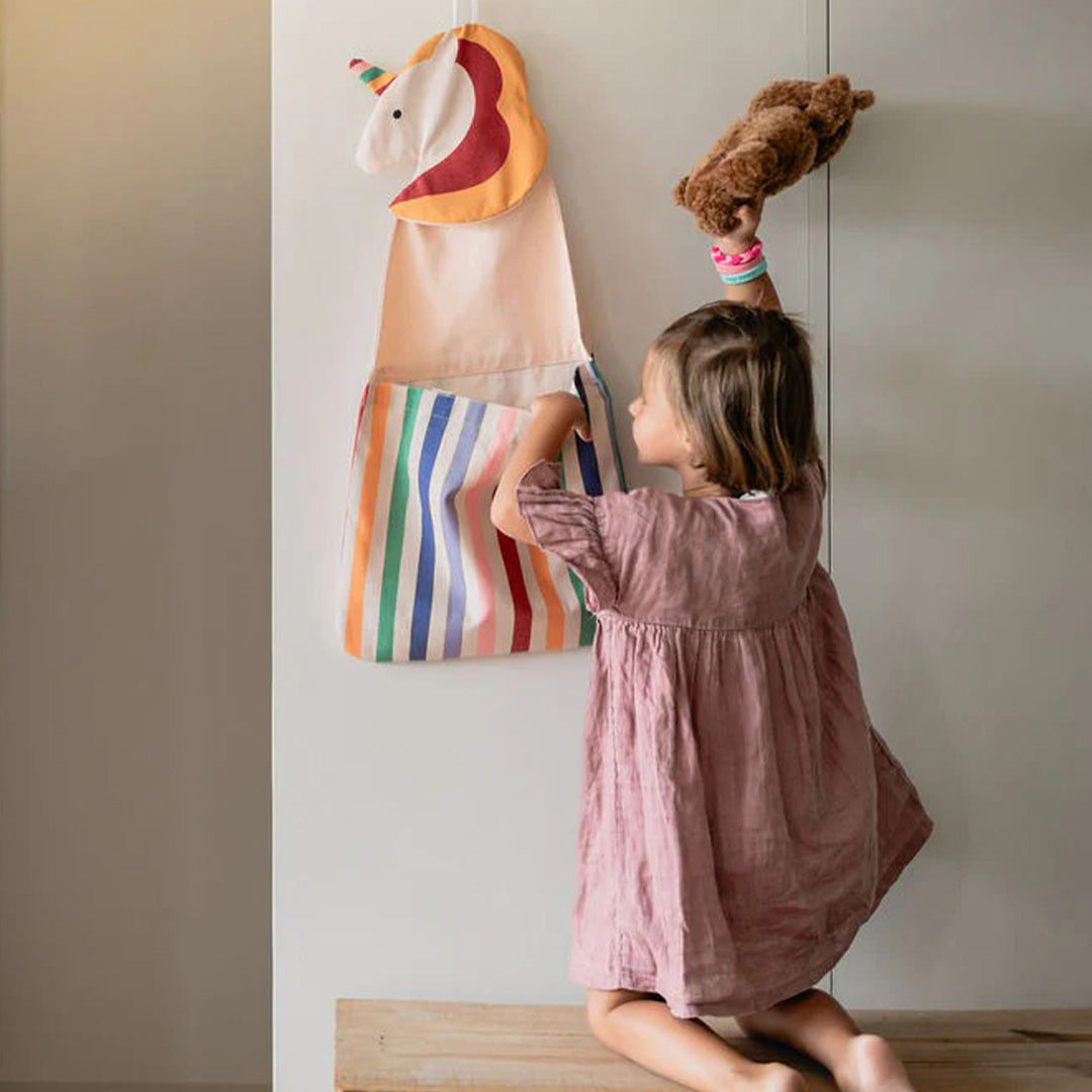 Een kind stopt een teddybeer in de play&go eenhoorn wandopberger en draagtas.