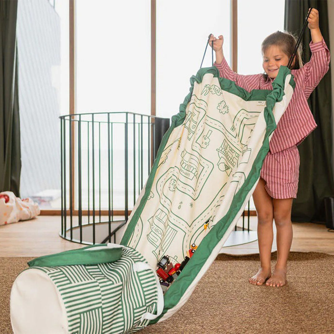 Een kind trekt het play&go speelkleed met wegenkaart omhoog om speelgoed in de opbergmand te verzamelen.