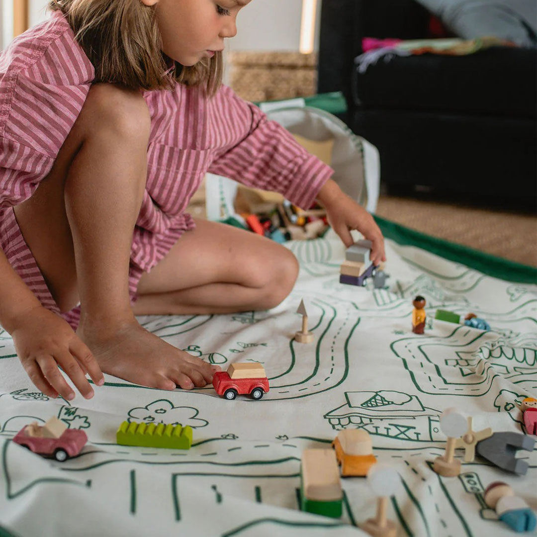 Een kind speelt met houten speelgoedauto's op het play&go speelkleed met wegenkaart.