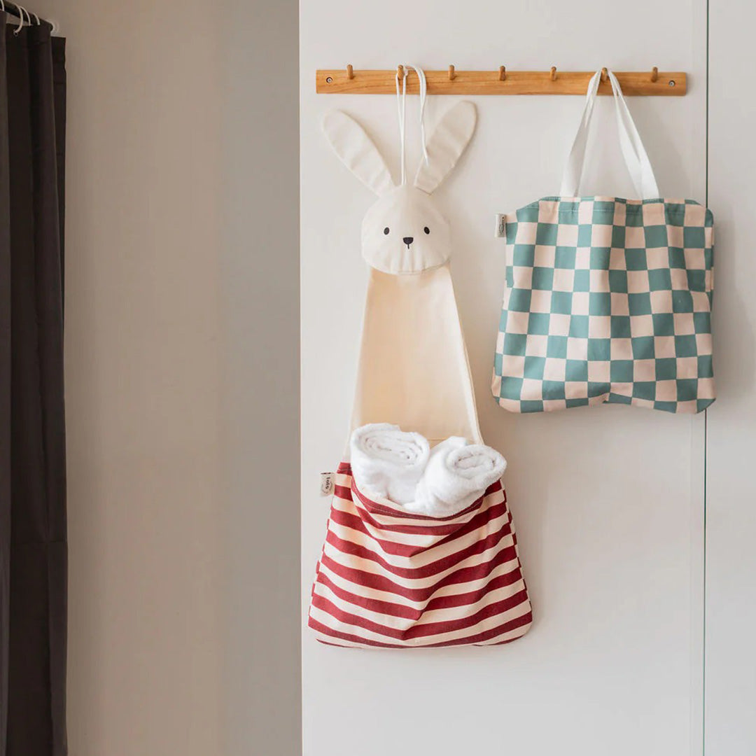 De play&go konijnen wandopberger met opgerolde handdoeken hangt aan een houten rek naast een geruite draagtas.