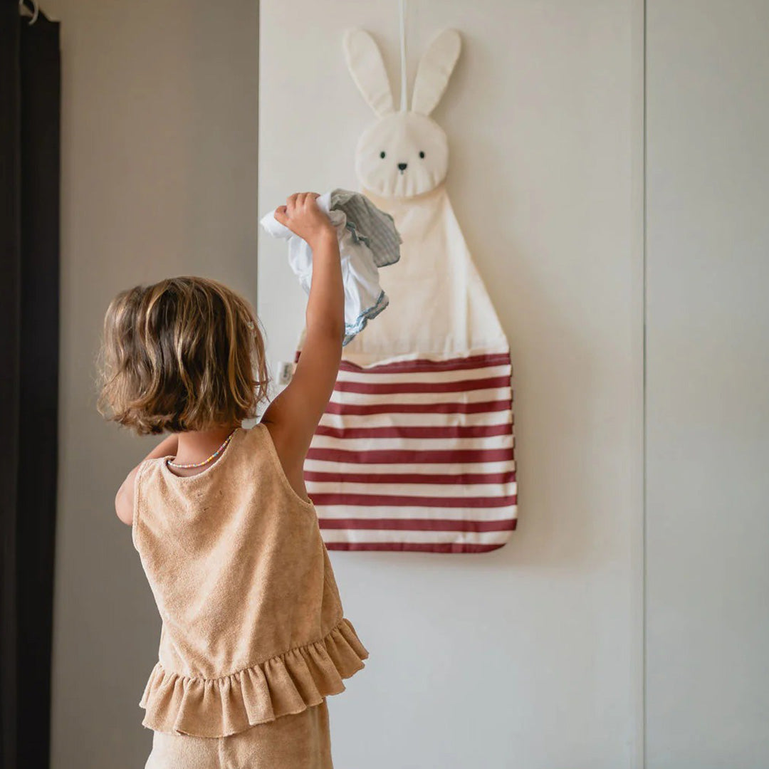 Een kind stopt een doek in de play&go konijnen wandopberger die aan een witte muur hangt.