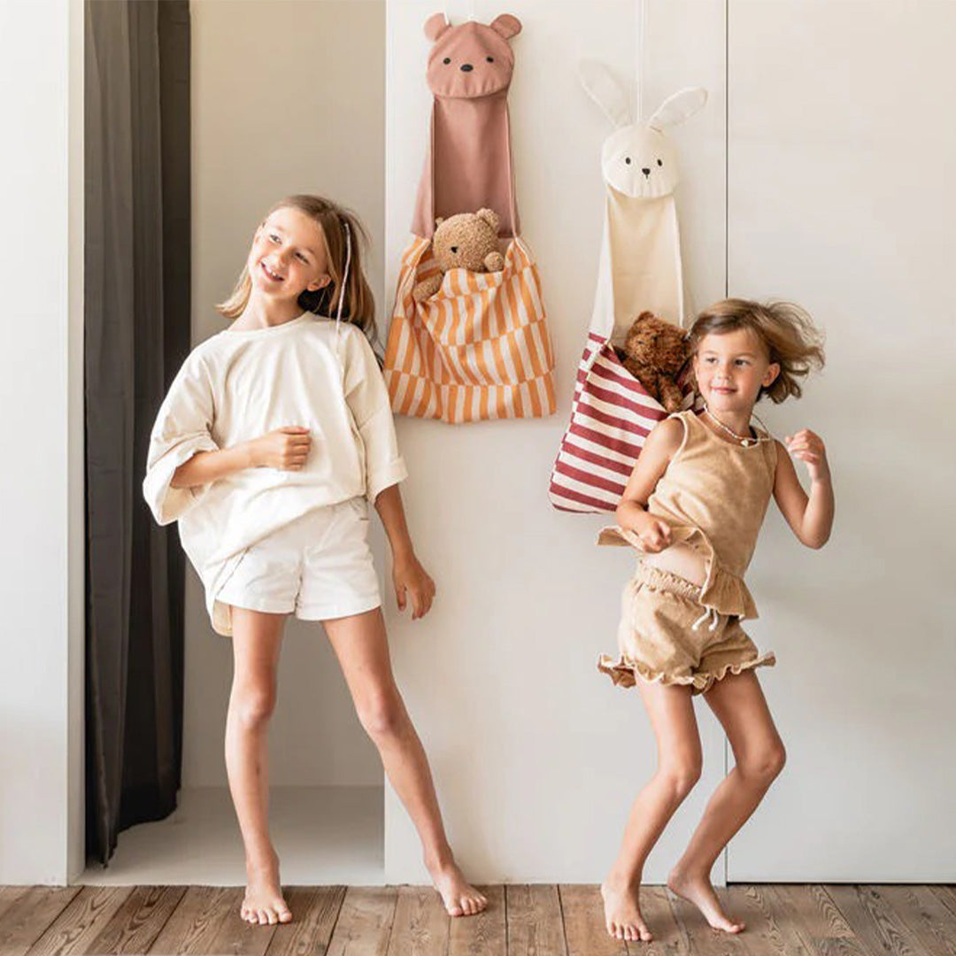 Twee meisjes spelen voor een muur met hangende play&go wandopbergers in de vorm van een beer en een konijn.