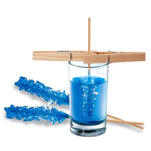 Een demonstratie van kristallen kweken met een glas blauwe vloeistof en blauwe kristalsuikerstokjes.