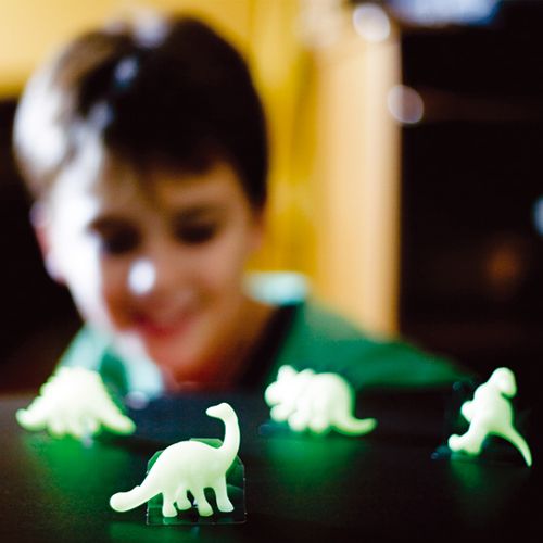 Een kind kijkt naar verschillende lichtgevende 3D dinosaurusfiguren op een donkere ondergrond.