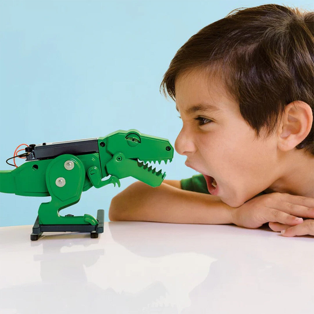Een jongen kijkt met open mond naar de groene 4M KidzRobotix T-Rex robot.