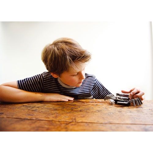 Een kind speelt met de zilverkleurige 4M KidzRobotix tafelblad robot op een houten tafel.