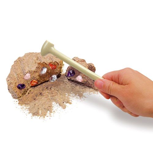 Een hand gebruikt een graafgereedschap om kleurrijke kristallen op te graven uit een beige blok van de 4M kristalmijn opgraafkit.