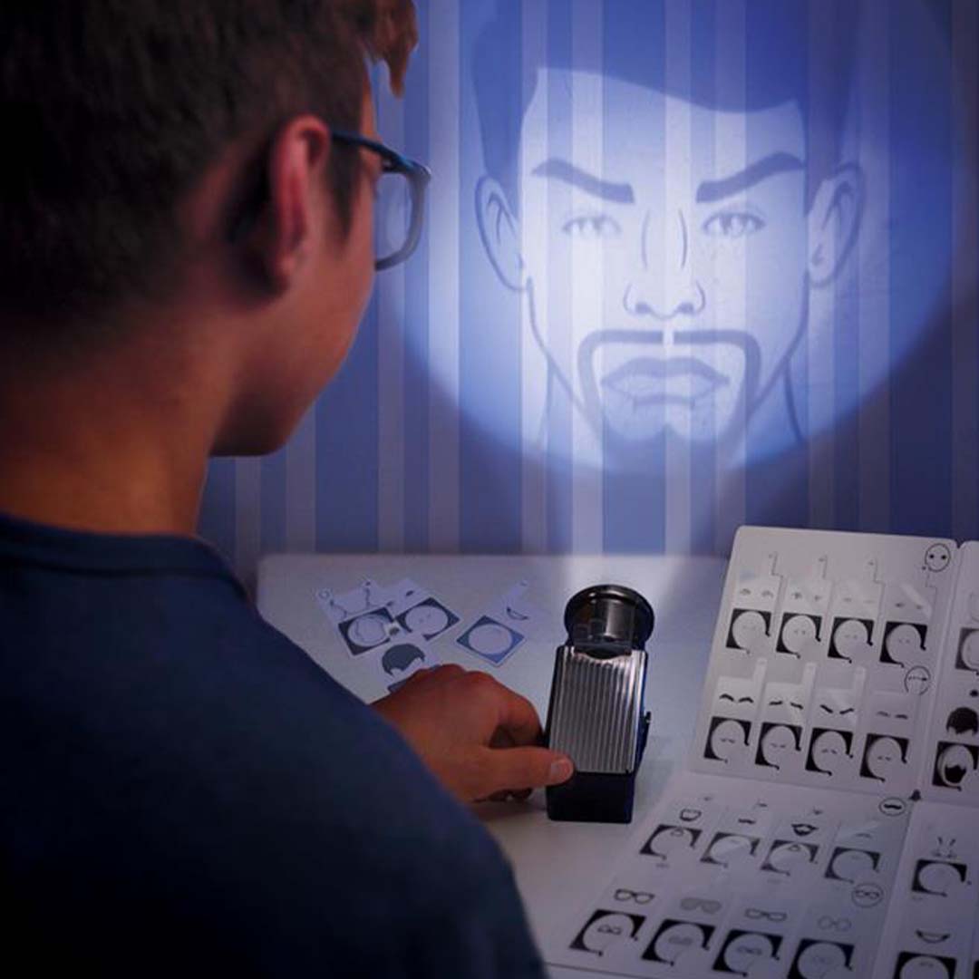 Een persoon gebruikt de projector van de detective kit om een gezicht op de muur te projecteren, met kaarten voor gezichtsherkenning op tafel.