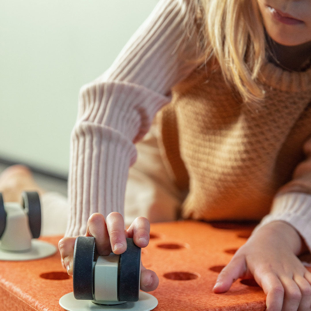 Een kinderhand houdt een modu wiel vast dat bevestigd is aan een oranje speelgoedblok.