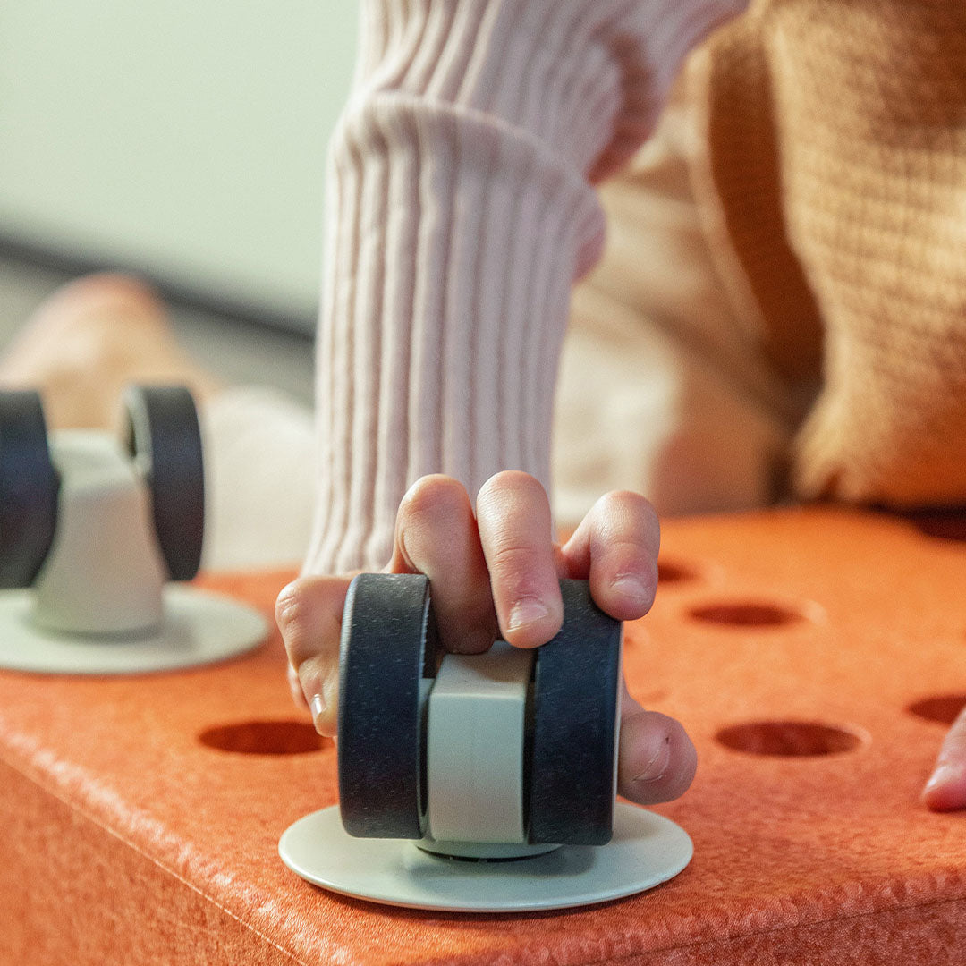 Een kinderhand houdt een Modu 360° wiel vast op een oranje speelstructuur.