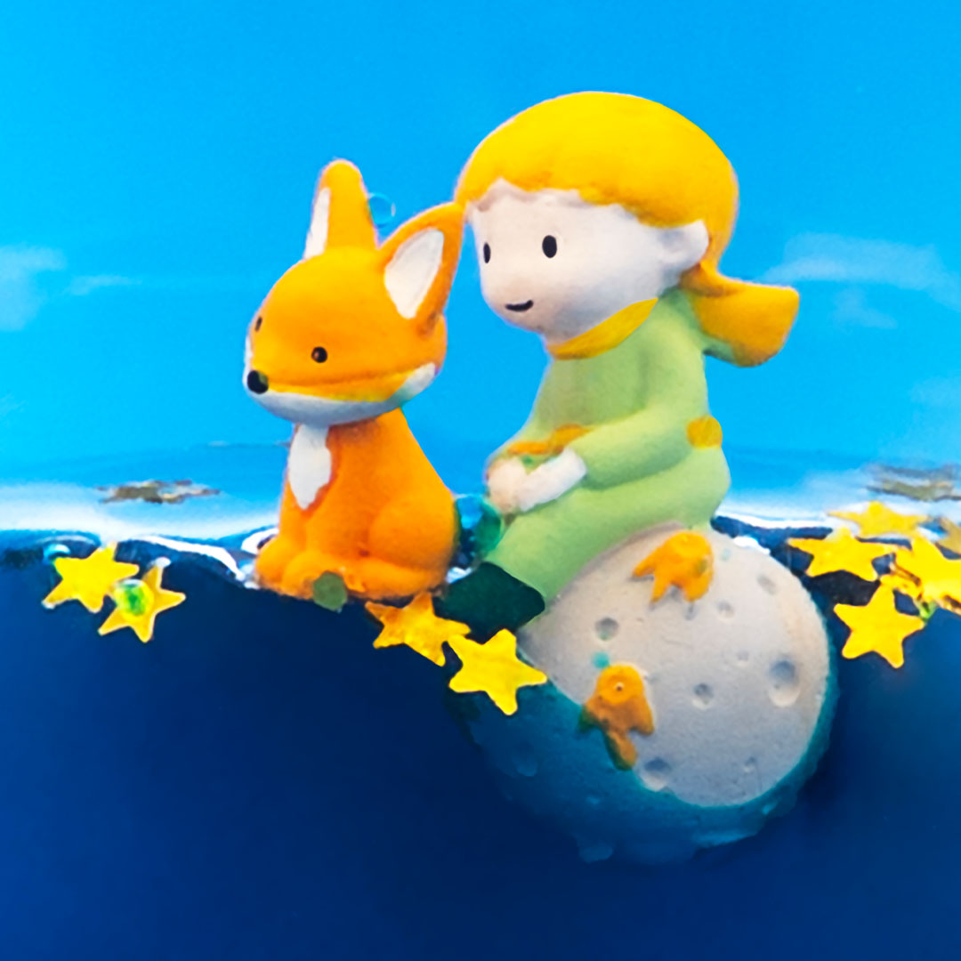 Detail van de Le Petit Prince figuren, een jongen en een vos, zittend op een maan tussen sterren.