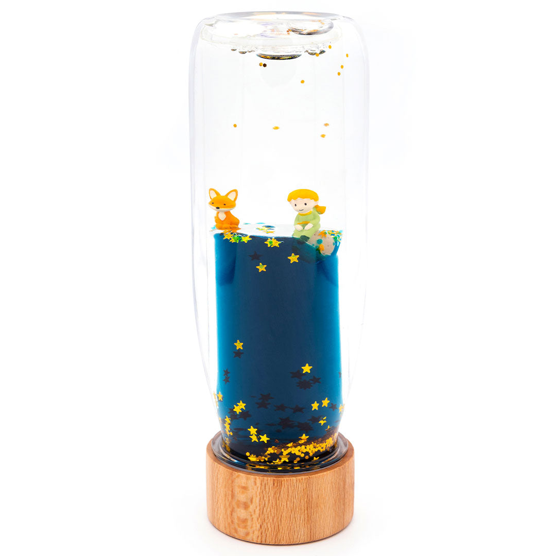 Petit Boum sensorische fles met Le Petit Prince figuren, blauwe vloeistof en sterren, op een houten voet.