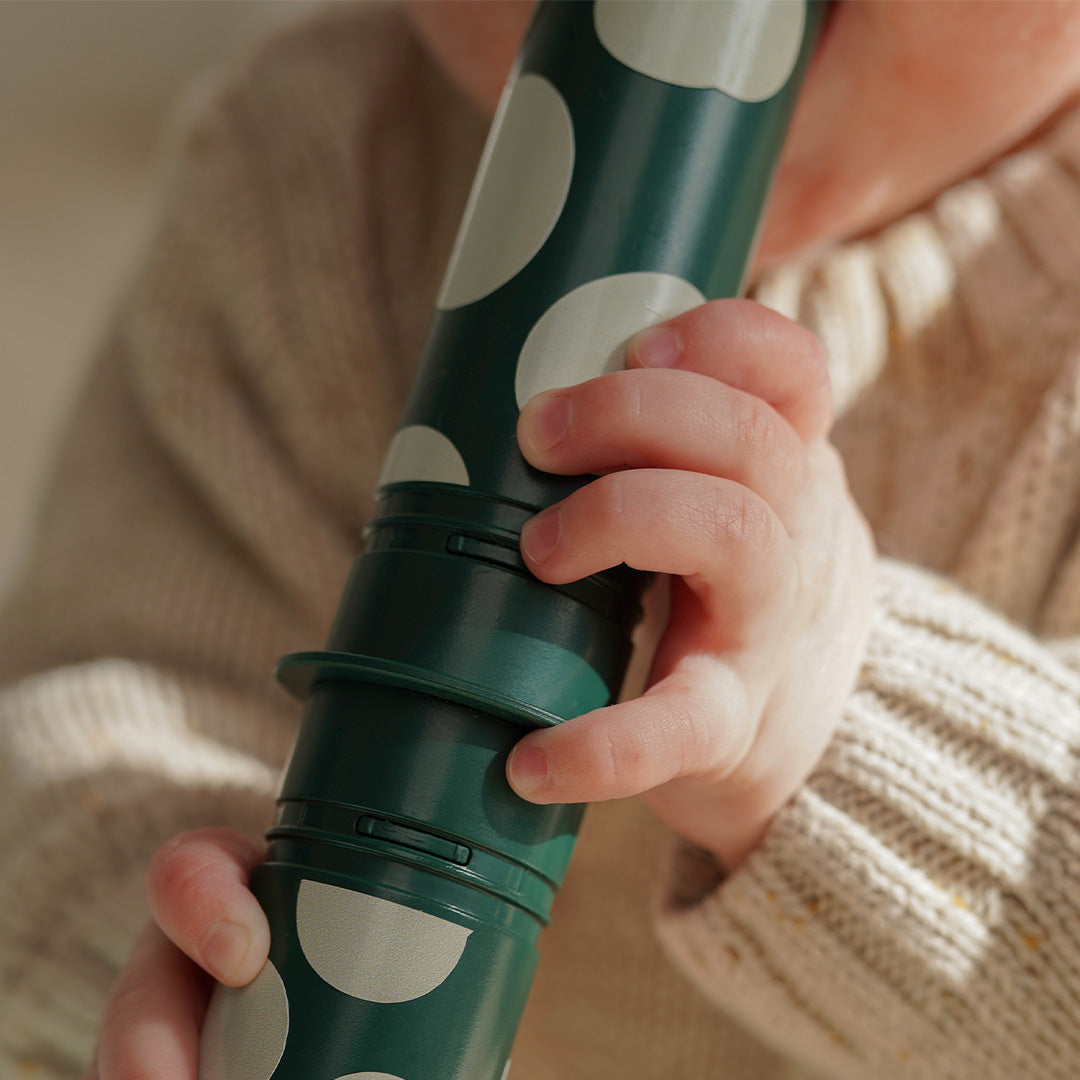 Een close-up van een babyhand die een groene Modu rammelaarpin met witte stippen vasthoudt.