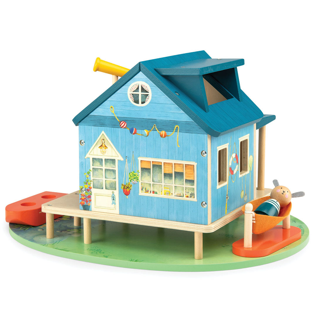 Achterkant van het Moulin Roty houten poppenhuis 'huis aan het meer' met een konijnenfiguur in een oranje hangmat.