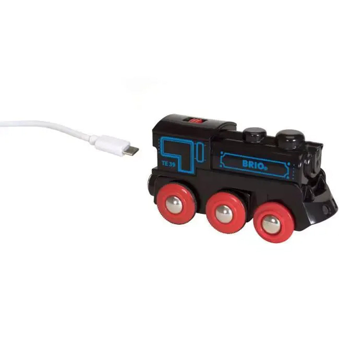 Brio oplaadbare speelgoedlocomotief met rode wielen, aangesloten op een witte USB-C oplaadkabel.