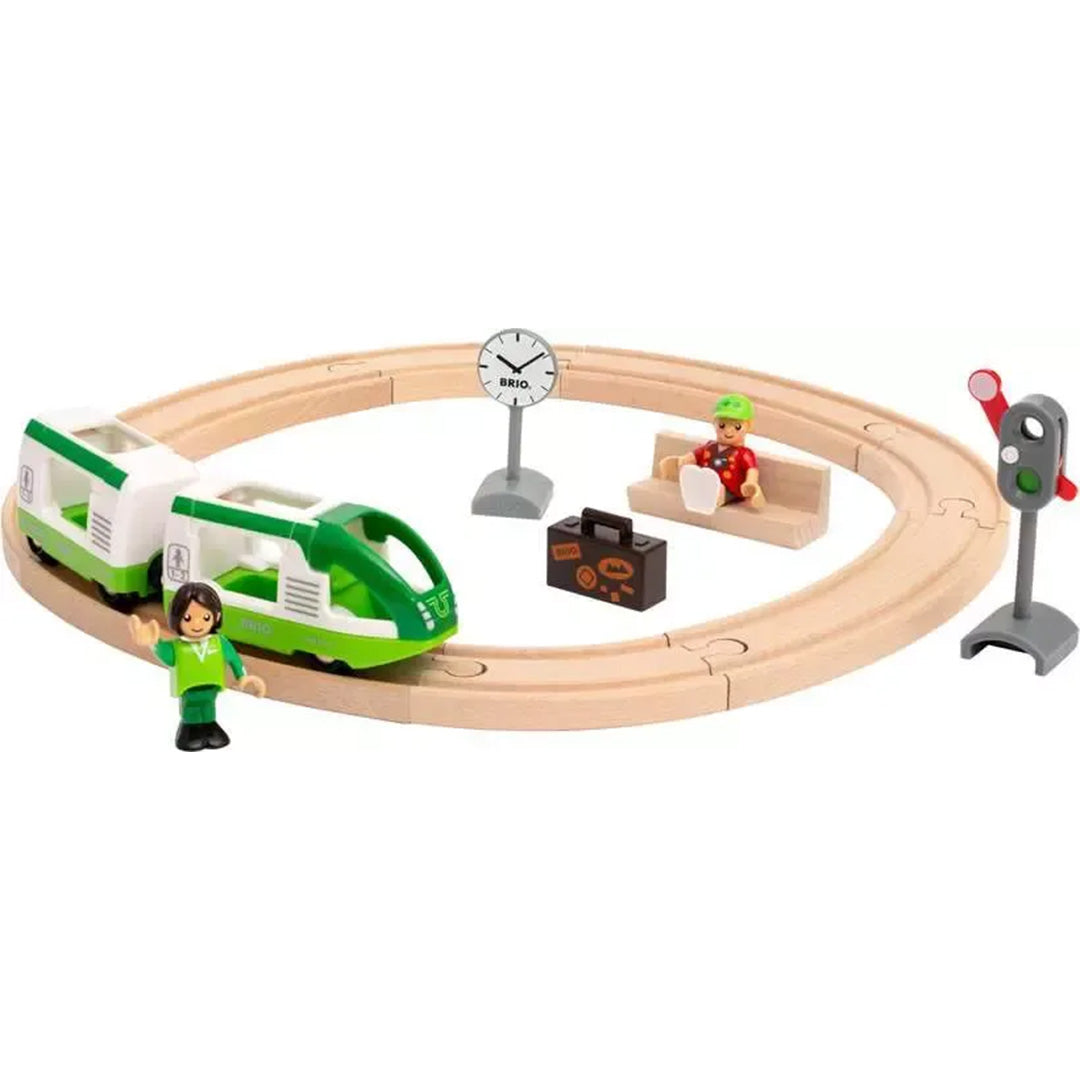 Brio treinbaan cirkel met groene trein, twee figuren, een bankje, klok en sein op een houten spoor.