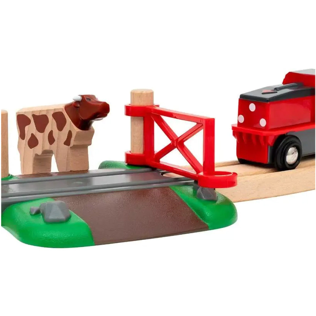 Detail van een houten koe bij een rode spoorwegovergang en een rode trein op de Brio treinbaan.
