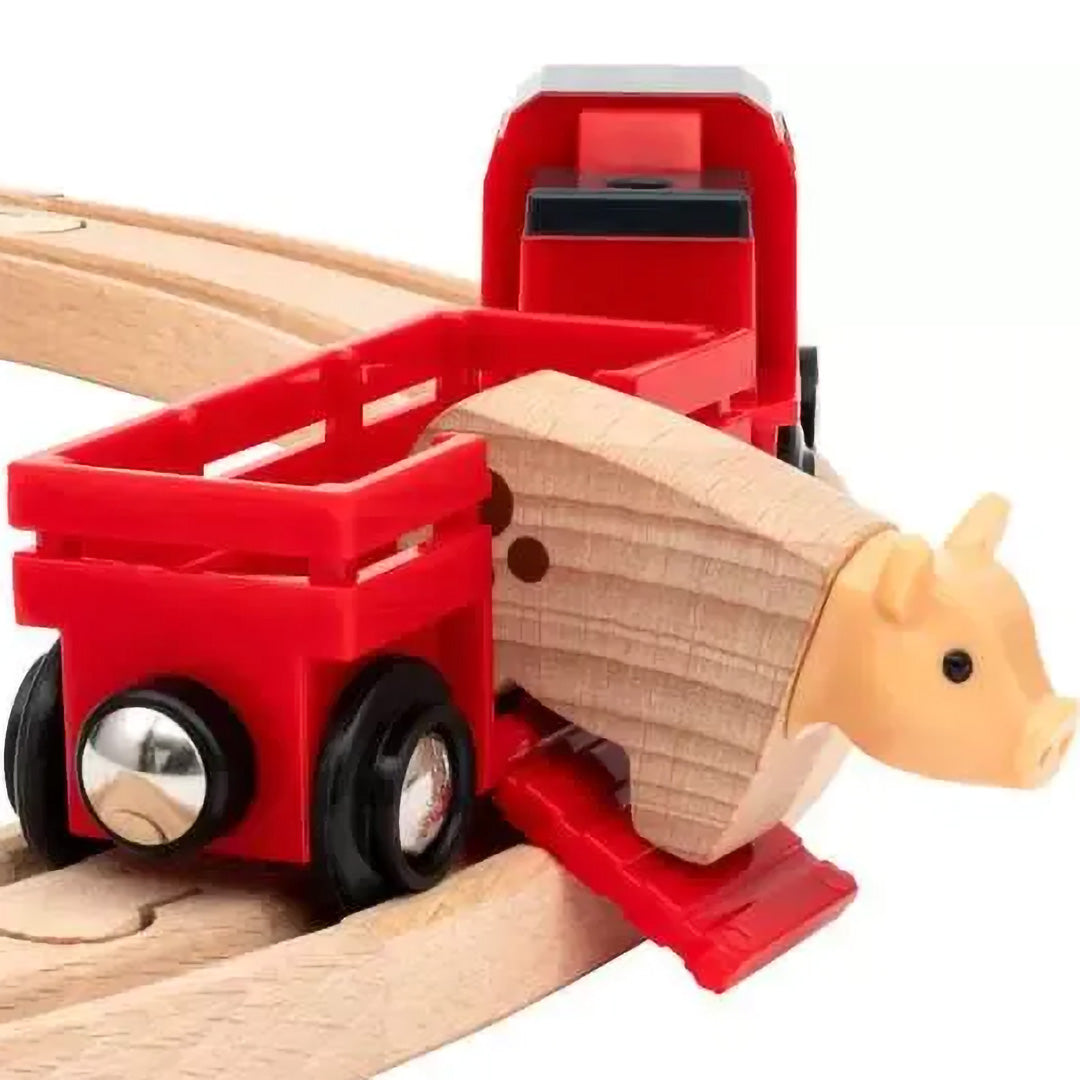 Detail van een Brio rode treinwagon met een houten varken, gekoppeld aan een rode locomotief op de houten treinbaan.