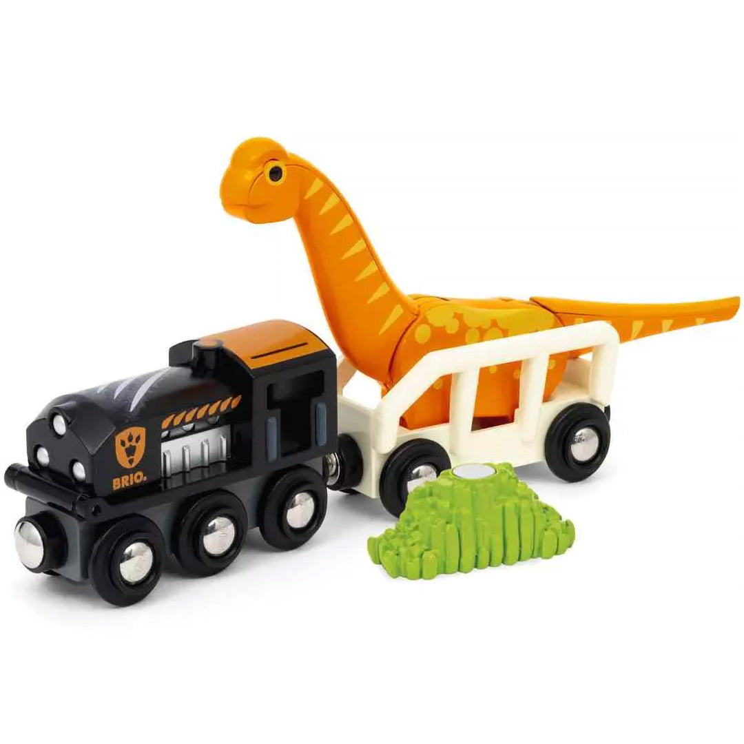 Brio speelgoedtrein met een zwarte locomotief en een wagon die een oranje dinosaurus vervoert, naast een groene struik.