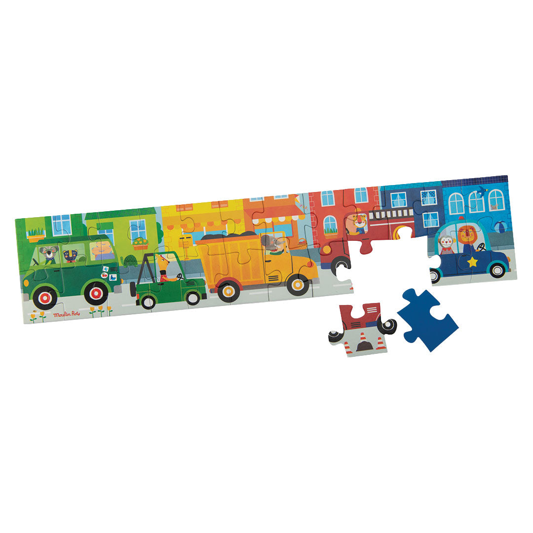 Een deels in elkaar gezette Moulin Roty voertuigenpuzzel van 24 stukjes met een straatbeeld en losse puzzelstukken.