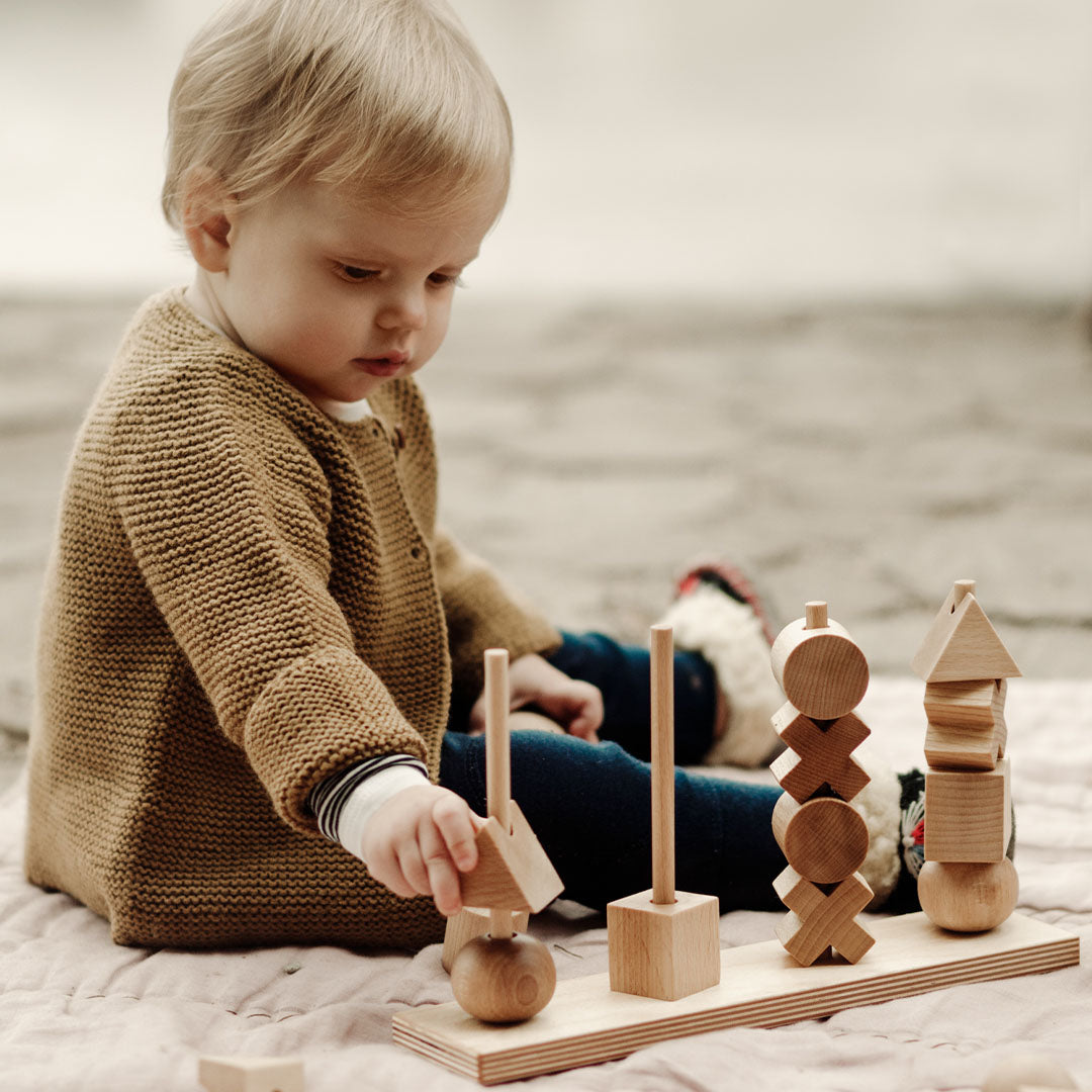 Een baby plaatst een houten blok op een van de Wooden Story stapeltorens.