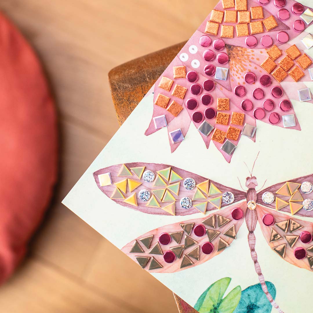 Detail van een onafgemaakte libelle mozaïekillustratie met roze, oranje en zilveren stickers.