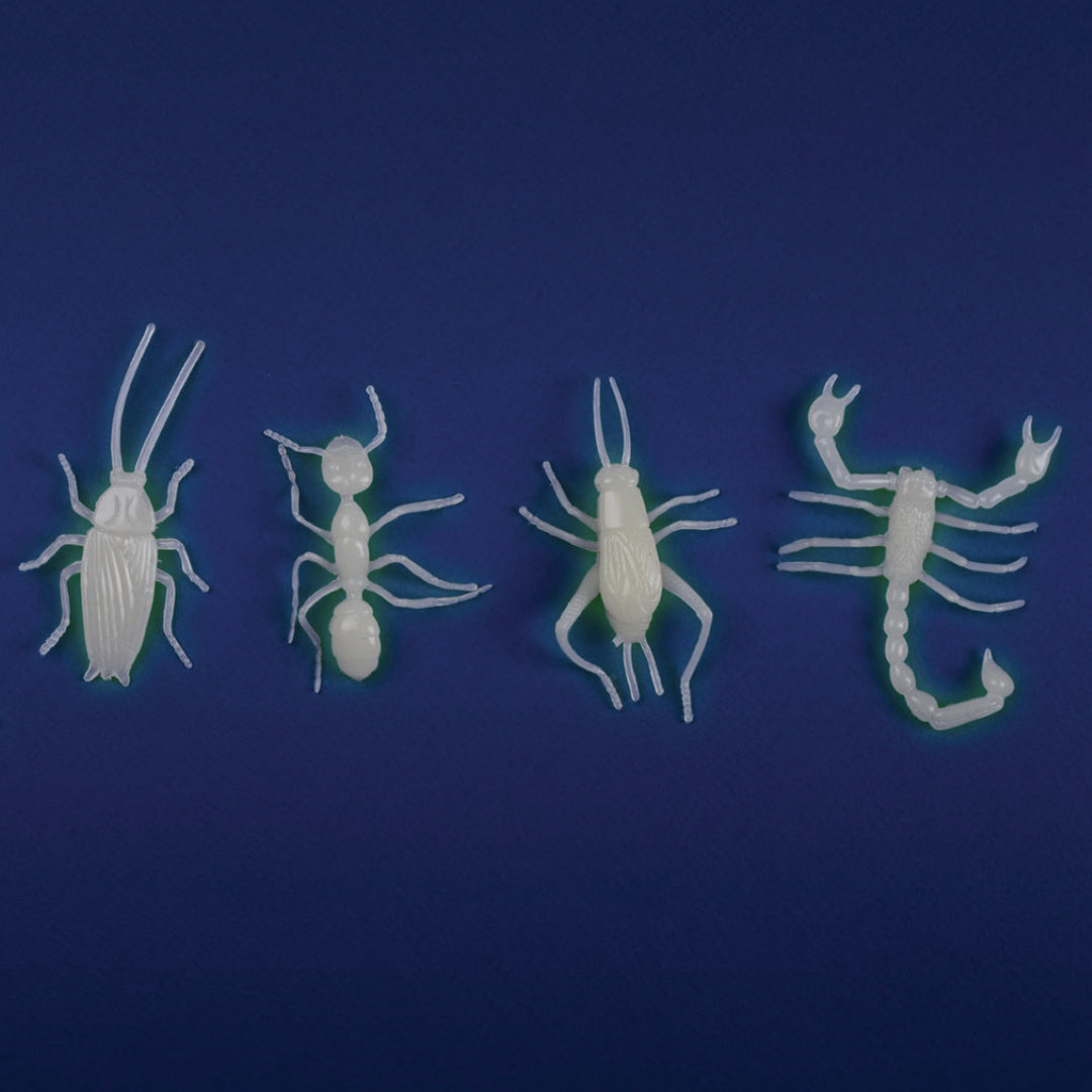 Vier glow in the dark insectenfiguurtjes, waaronder een mier en schorpioen, liggen op een donkerblauwe achtergrond.