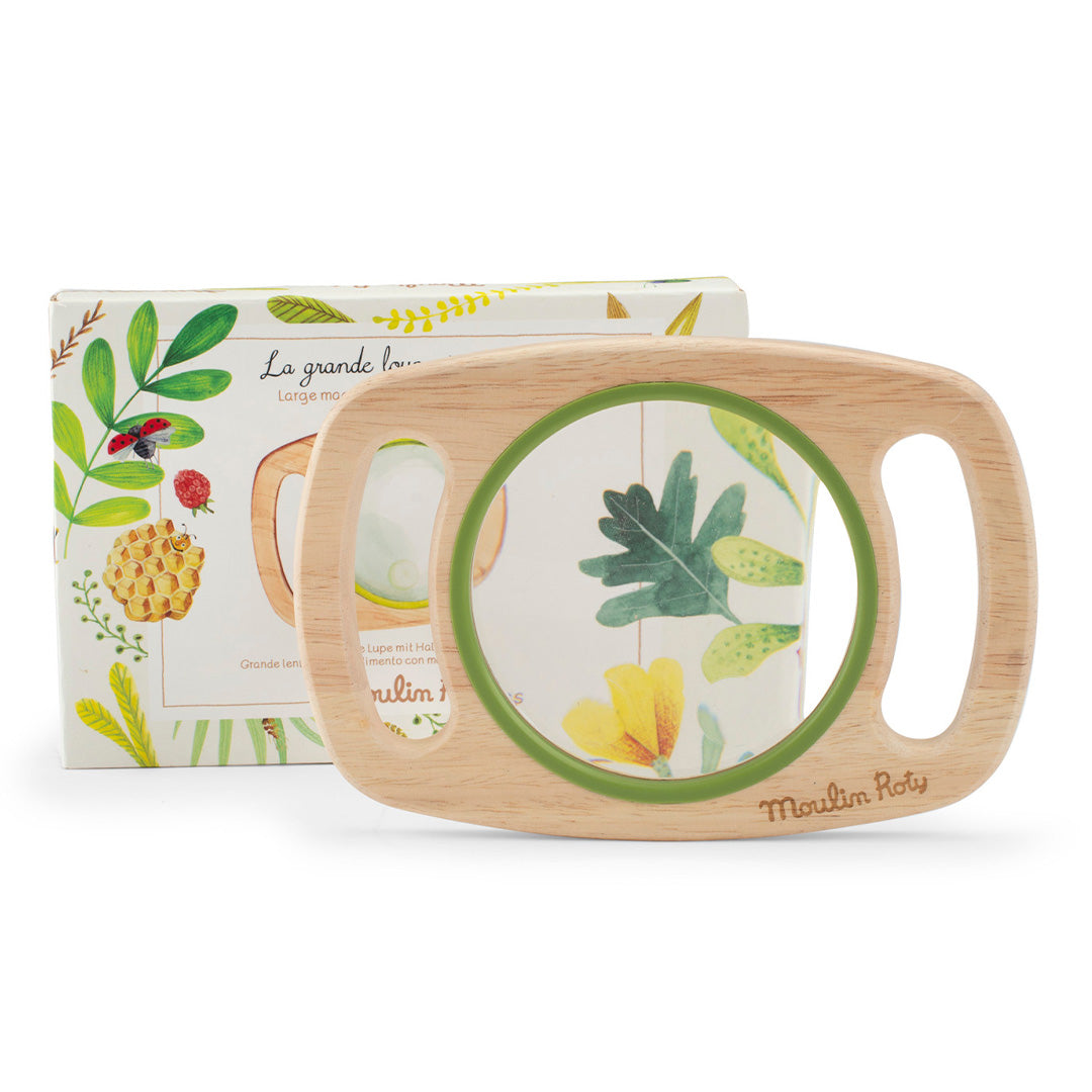Moulin Roty houten vergrootglas met groene rand en handvatten, met de botanisch geïllustreerde verpakking erachter.