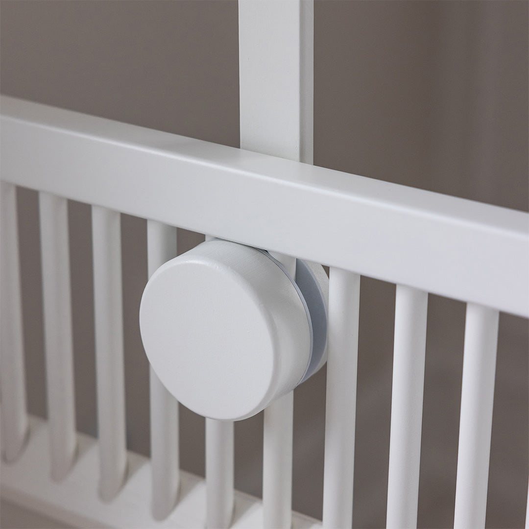 Detail van de witte houten mobielhouder van Sebra die aan de spijlen van een babywieg is bevestigd.