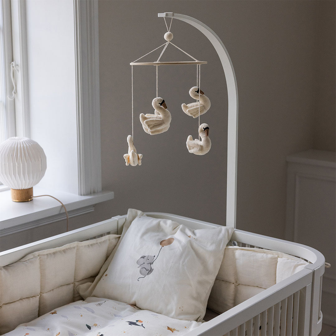 Sebra witte houten mobielhouder bevestigd aan een babywieg met een mobiel van zwanen erboven.