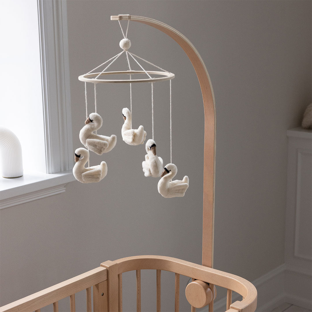 Sebra houten mobielhouder bevestigd aan een babywieg, met een mobiel van vijf witte zwanen.
