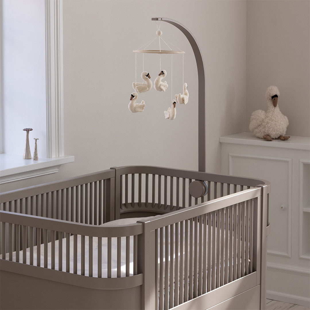 Sebra houten mobielhouder met een mobiel van zwanen bevestigd aan een grijze babywieg in een kinderkamer.