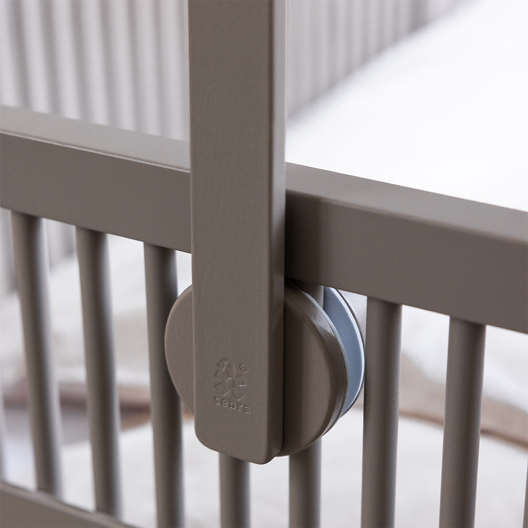Detail van de Sebra houten mobielhouder bevestigd aan de spijlen van een babywieg, met het Sebra logo zichtbaar.