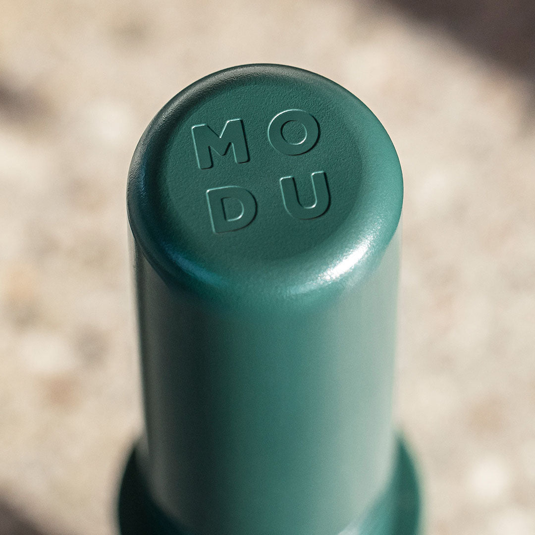 Detailfoto van de bovenkant van een donkergroene Modu verbindingspin met het Modu logo.