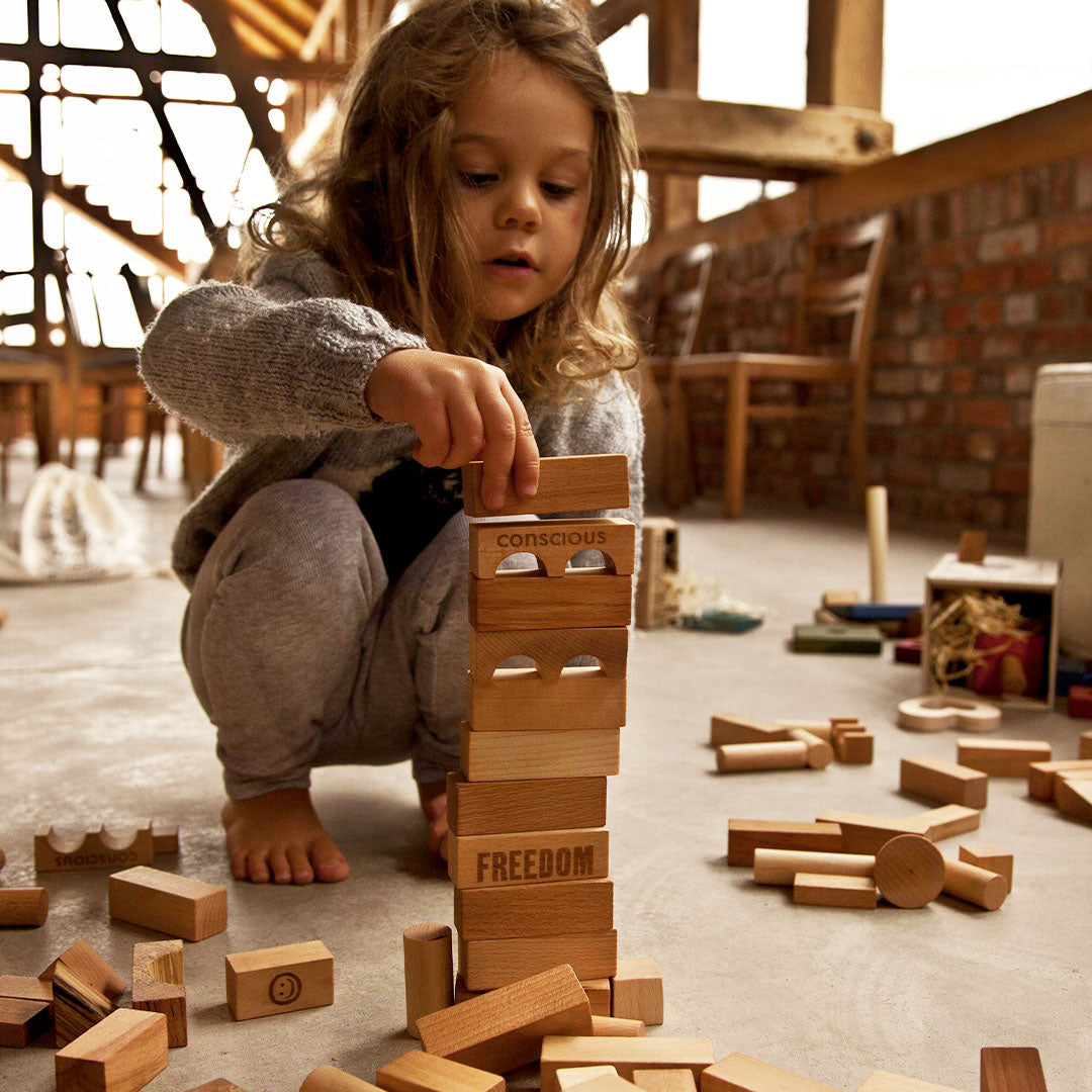 Een kind bouwt een toren met Wooden Story houten bouwblokken met tekst erop.