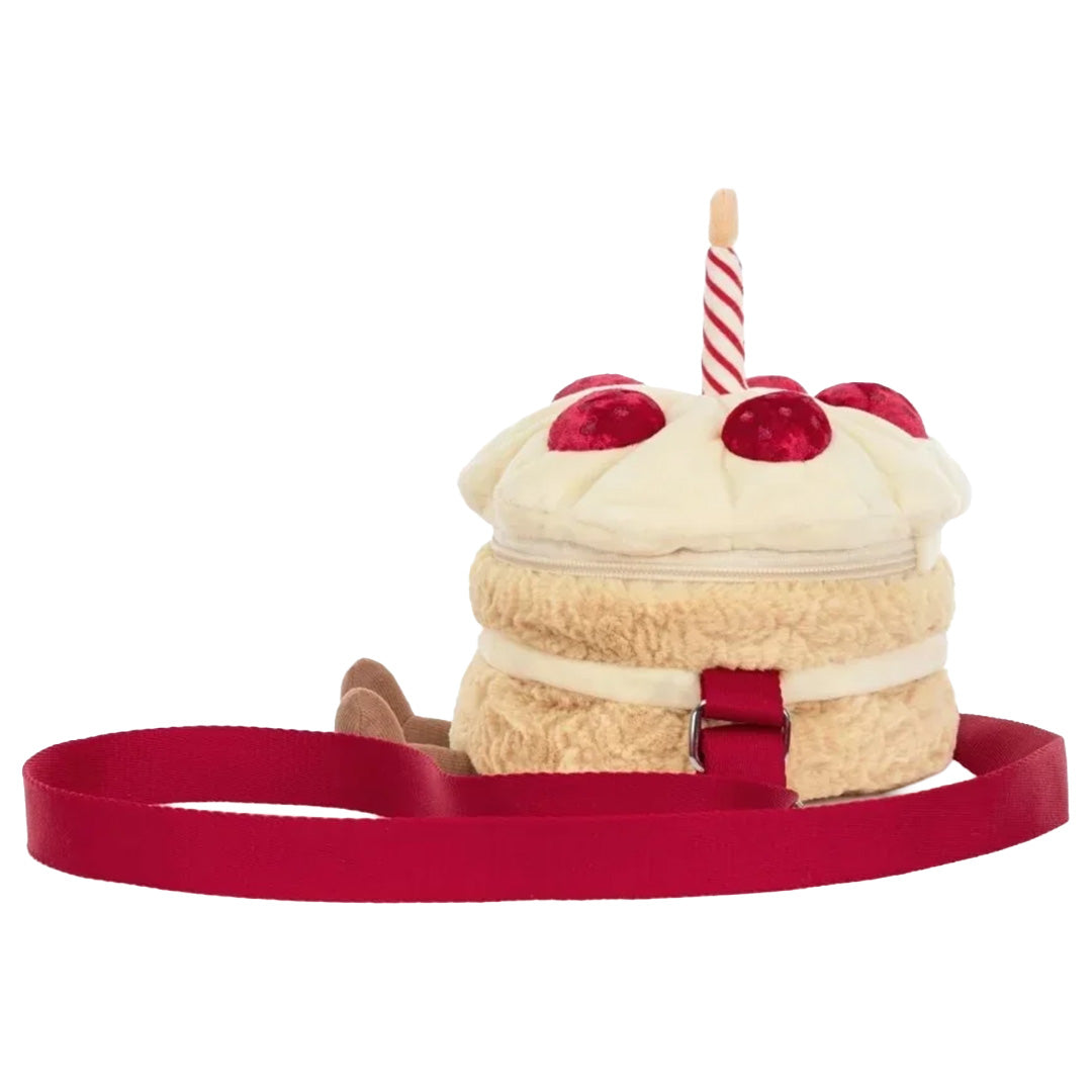 Jellycat kinder crossbodytas in de vorm van een verjaardagstaart met kaars en rode band, van de zijkant gefotografeerd.