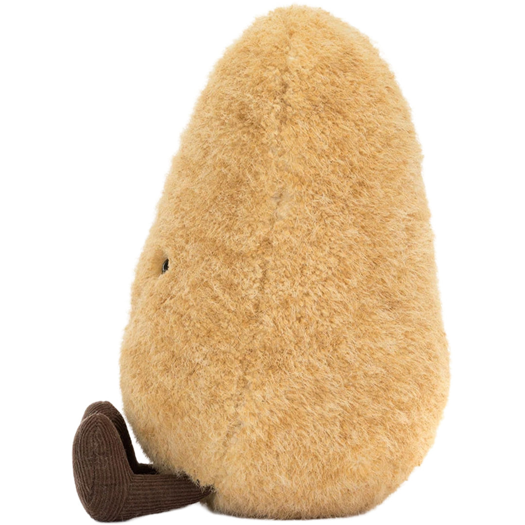 Zijaanzicht van de Jellycat knuffelaardappel Graham, beige, zittend met één bruine voet zichtbaar.