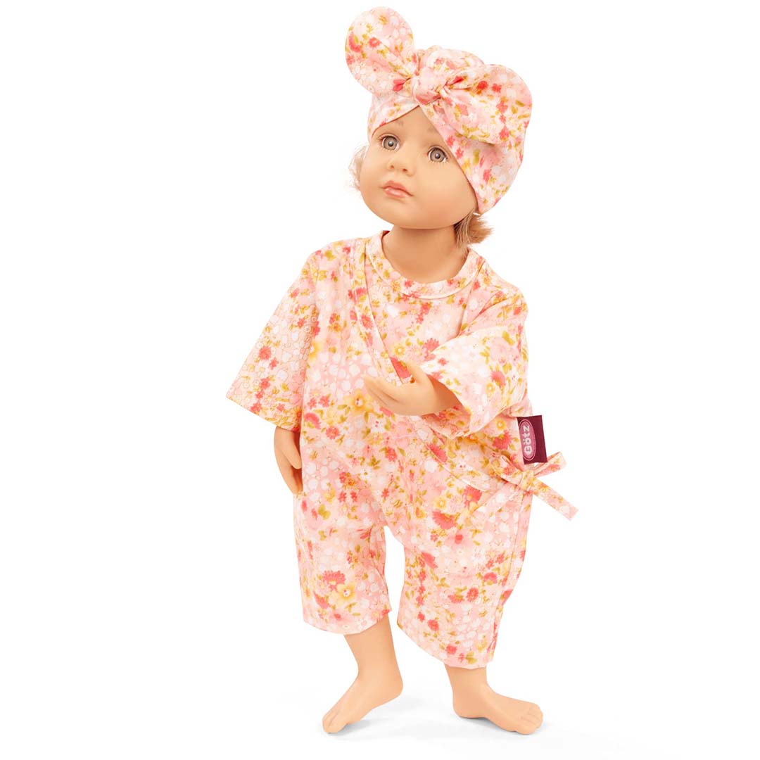 Gotz poppenkleding set met roze gebloemde jumpsuit en hoofdband gedragen door een staande pop.