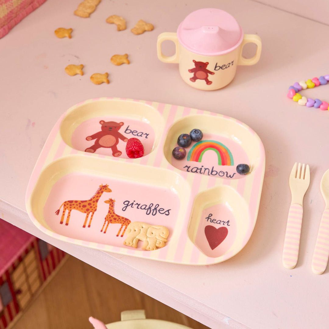 Het roze rice kinderservies met een verdeeld bord, beker en bestek, versierd met beren, giraffen, een regenboog en een hart.