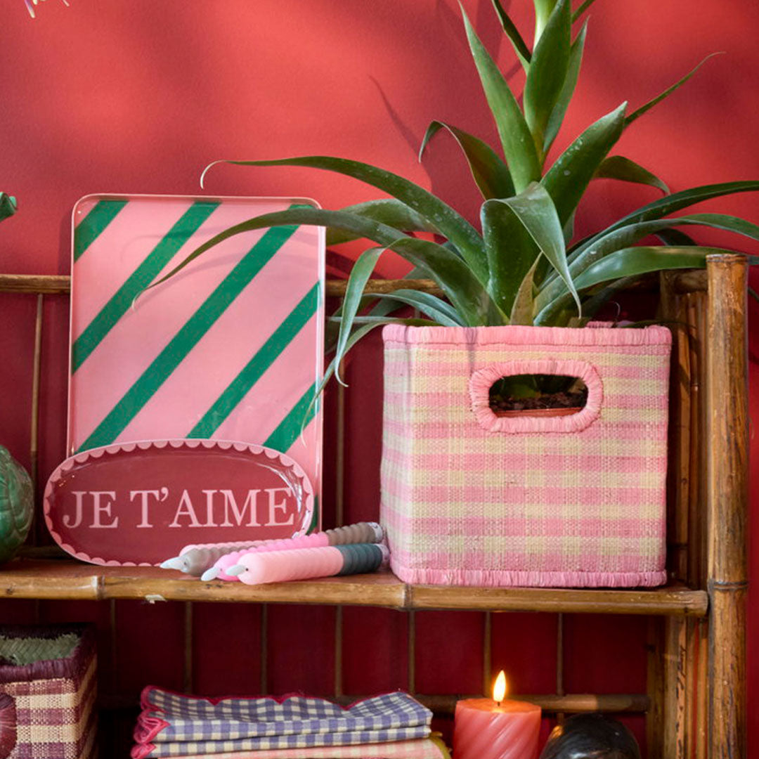 rice raffia opbergmand met roze ruitpatroon gebruikt als plantenpot op een houten plank.