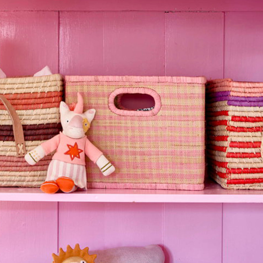 rice roze geruite raffia opbergmand op een roze plank naast een eenhoorn knuffel.
