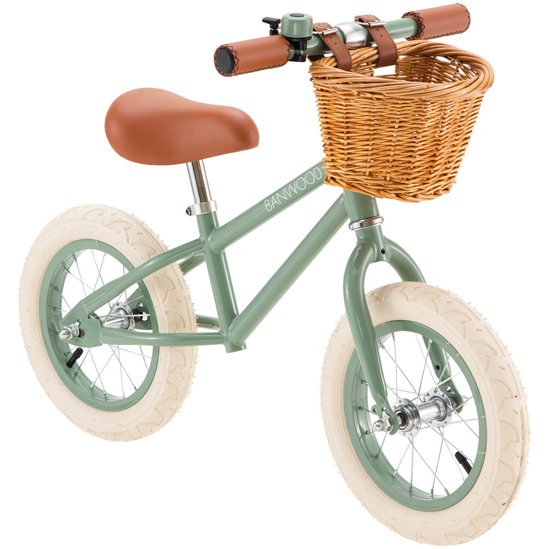 Banwood loopfiets in het groen met bruin zadel, handvatten en een rieten mandje aan het stuur.
