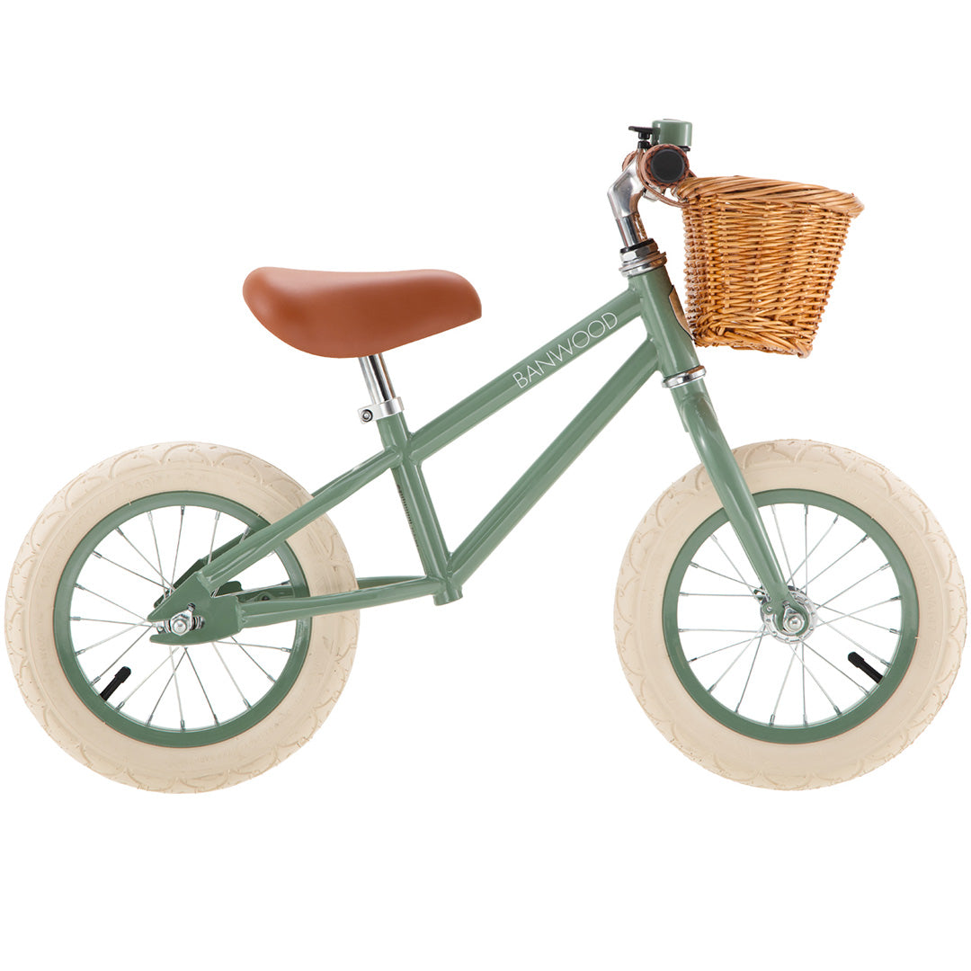 Zijaanzicht van de groene Banwood loopfiets met bruin zadel en een rieten mandje.