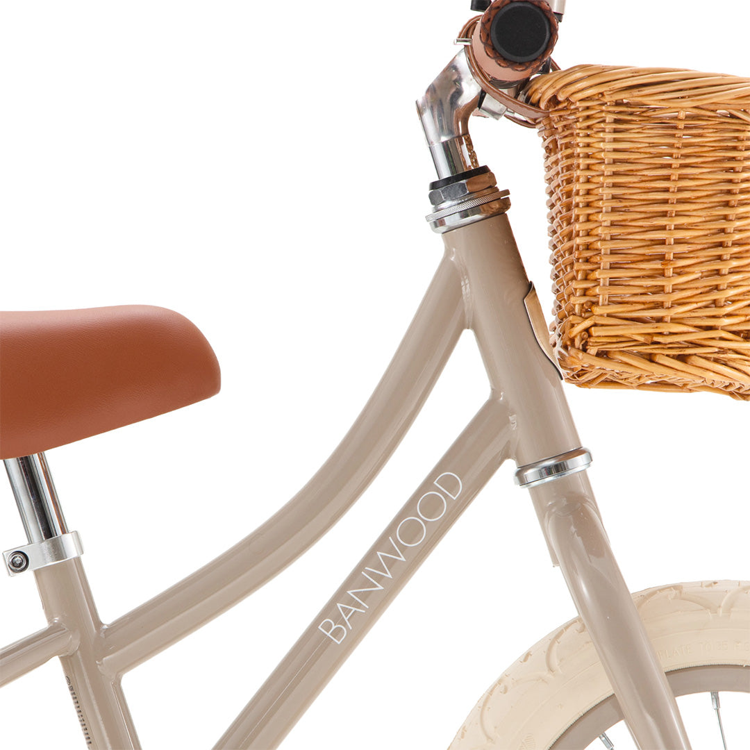 Detail van het beige frame van de Banwood loopfiets met logo en een deel van het rotan mandje.