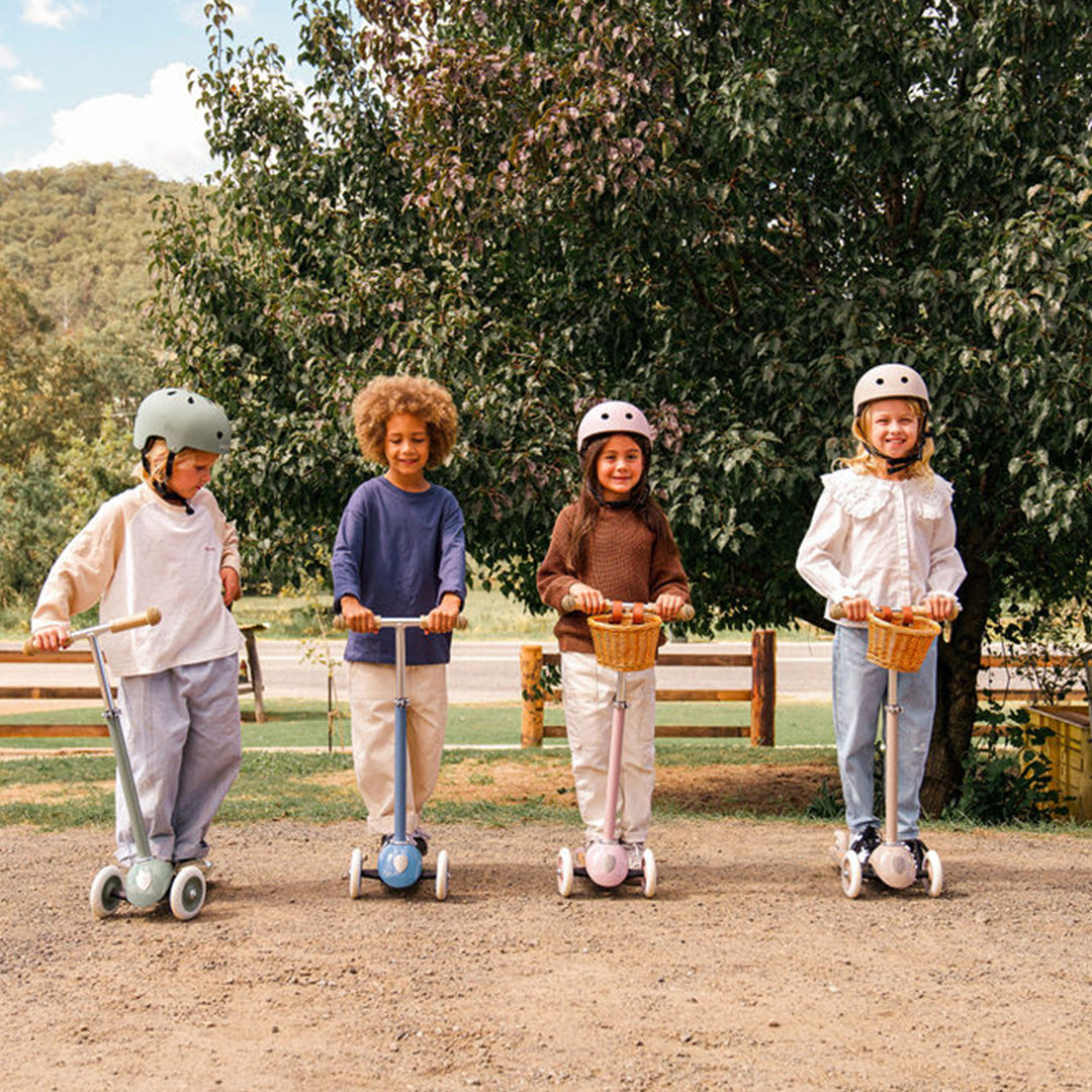 Vier kinderen met helmen staan buiten met hun Banwood kindersteps in verschillende kleuren.