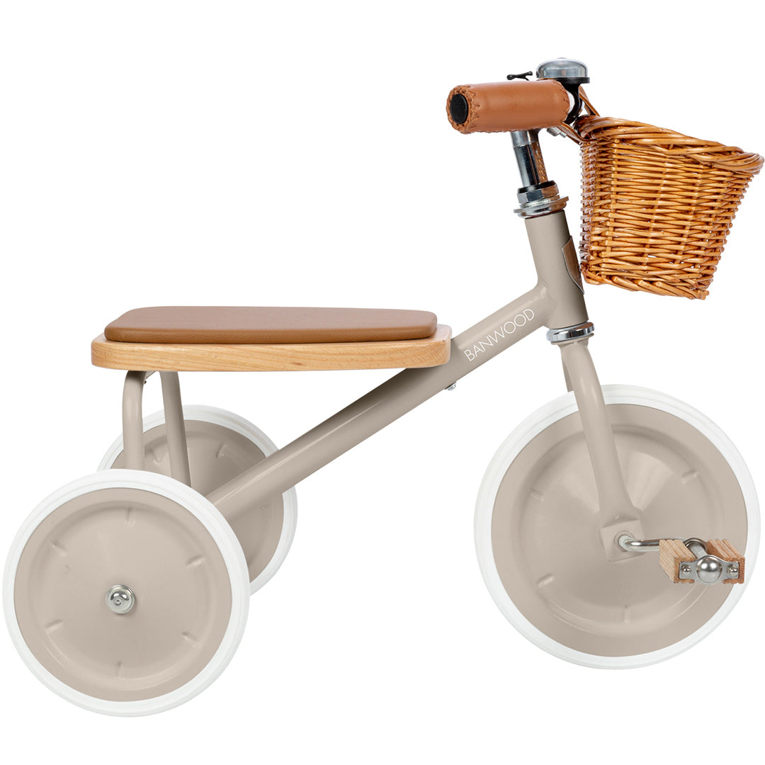 Banwood beige driewieler met bruin zadel en rieten mandje, schuin van voren gefotografeerd.