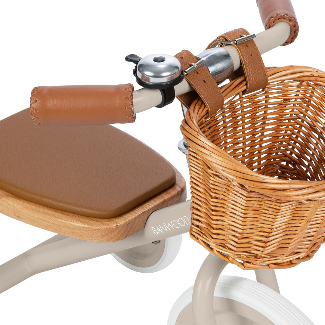 Detail van de Banwood beige driewieler met bruine handvatten, bel en rieten mandje.
