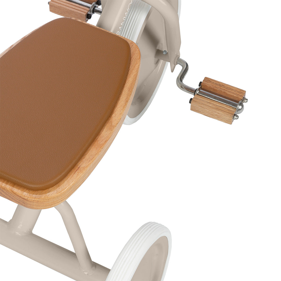 Detail van het bruine zadel en de houten pedalen van de Banwood beige driewieler.
