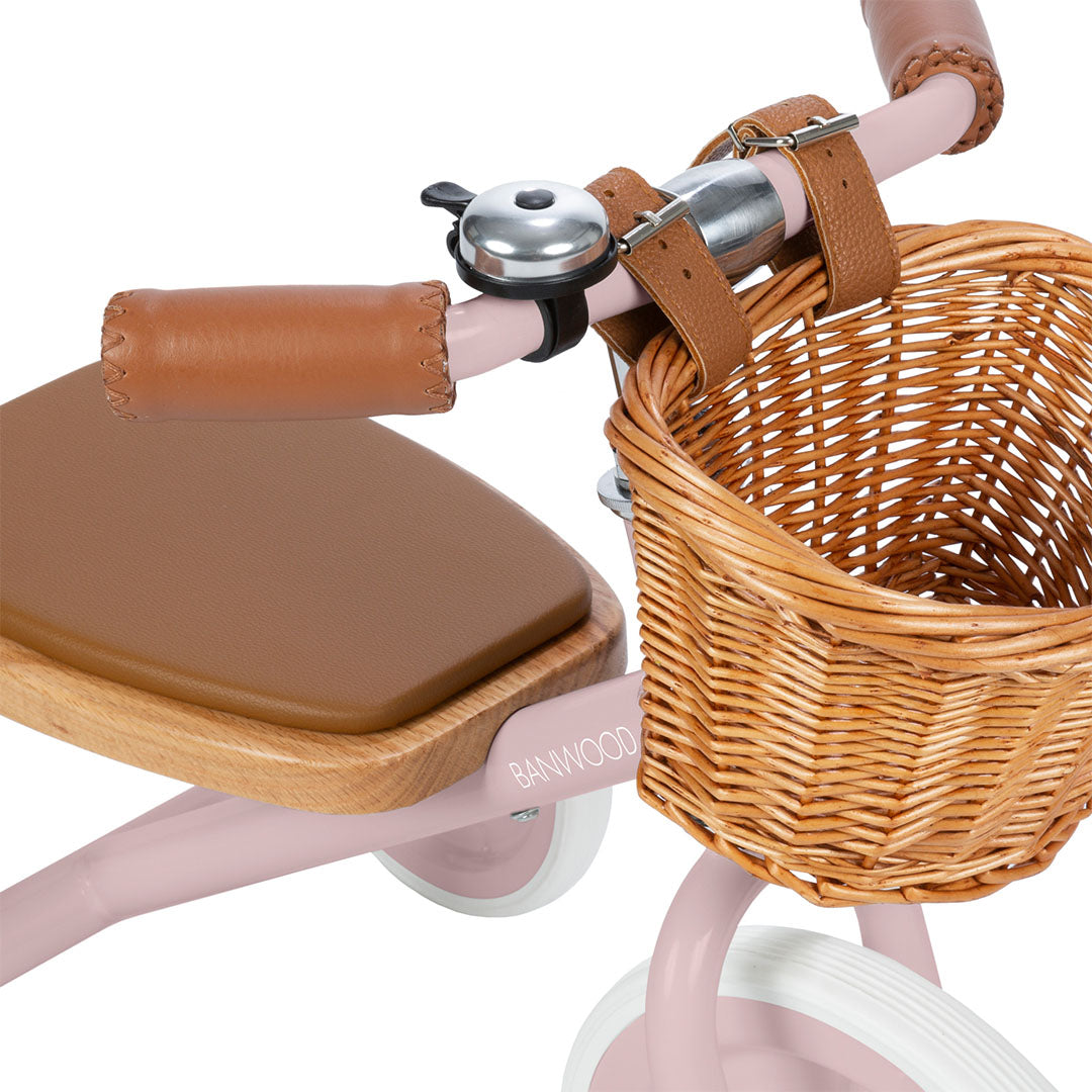 Detail van het stuur van de Banwood dusty roze driewieler met bruine leren handvatten, een bel en een rieten mandje.
