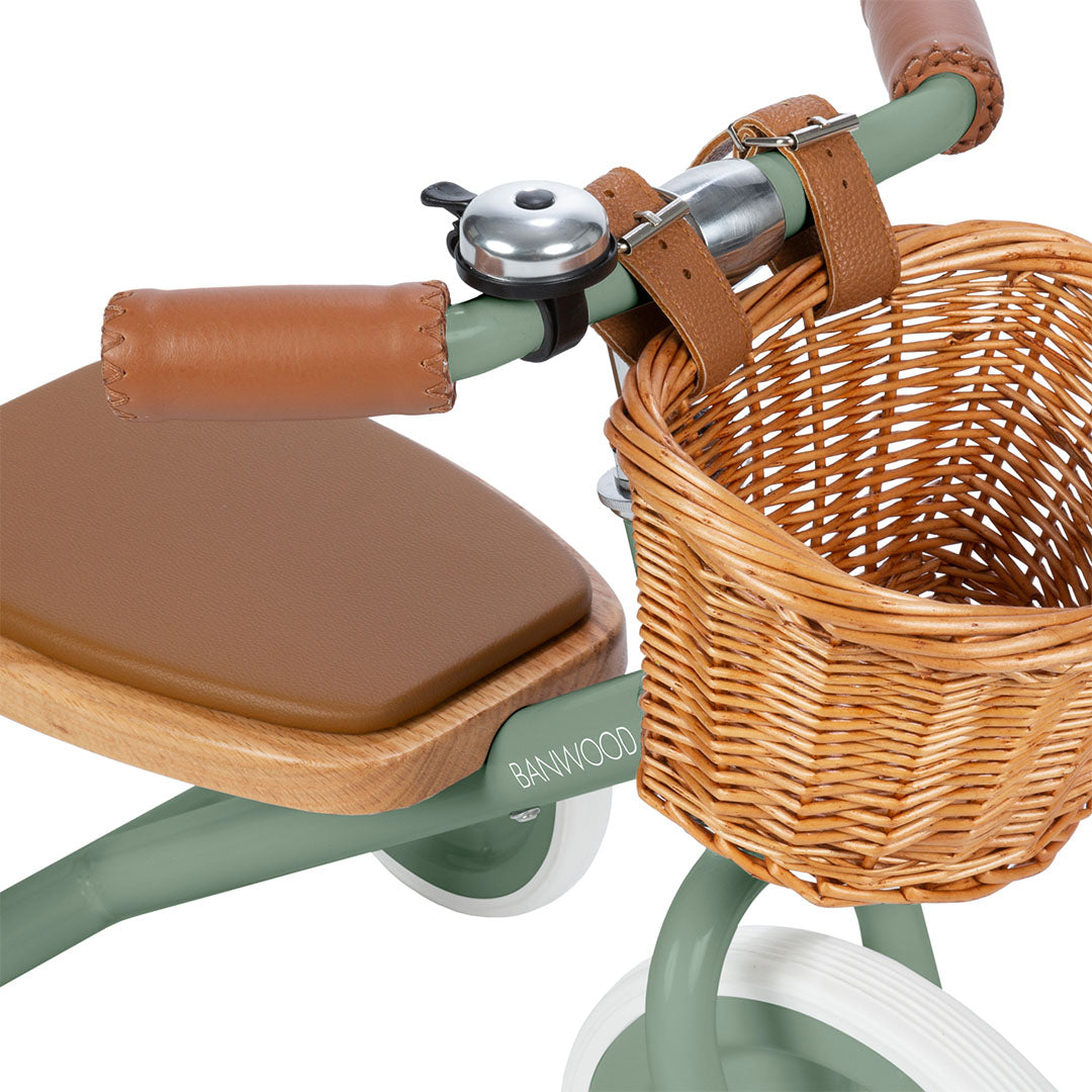 Detail van het stuur van de groene Banwood driewieler met bel, bruine handvatten en rieten mandje.